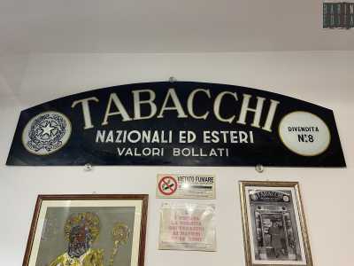 Il romano moderno � protagonista anche del logo pi� �recente� del Tabaccaio Di Monte, custodito all�interno del locale. La targa, in bianco e nero e risalente al 1943, presenta lo stile nella sua variante �raccordata�, ossia curva, quasi a voler imitare la forma di un semicerchio
